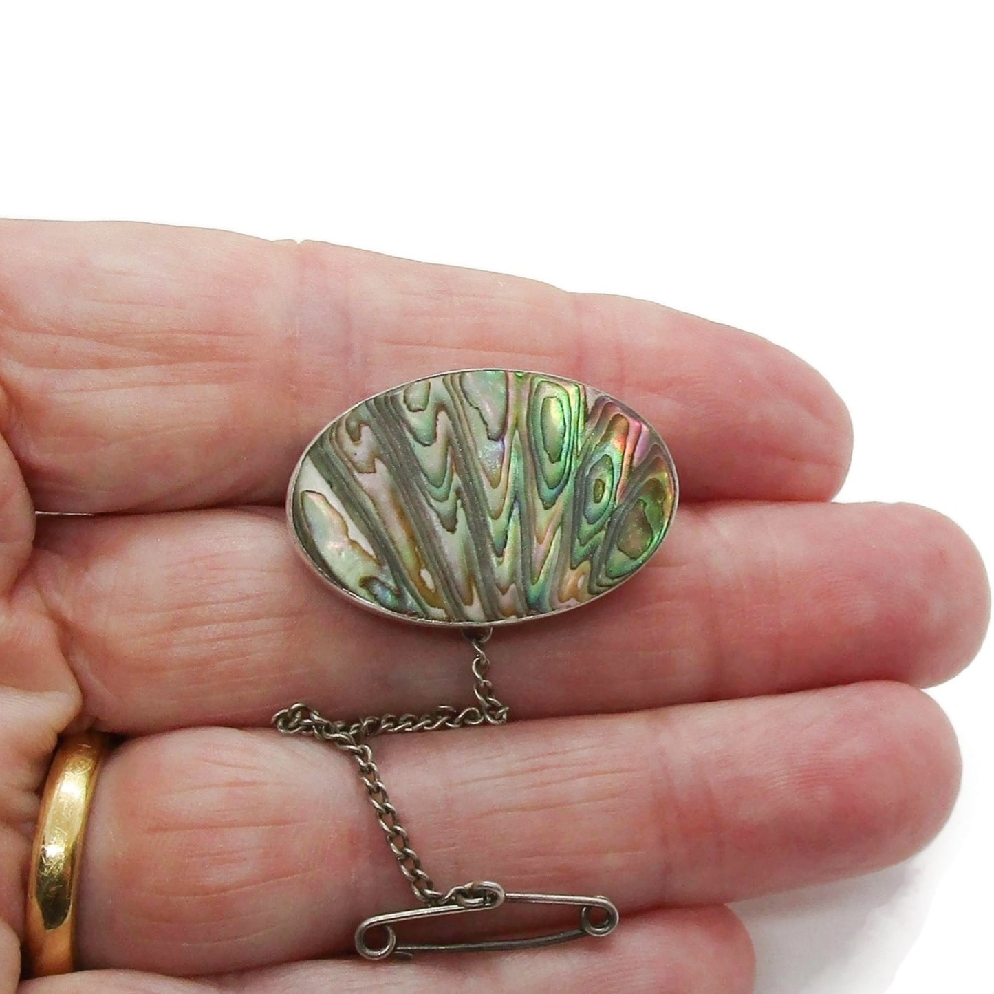 Oval sterling silver and carved paua shell brooch with safety chain held in hand