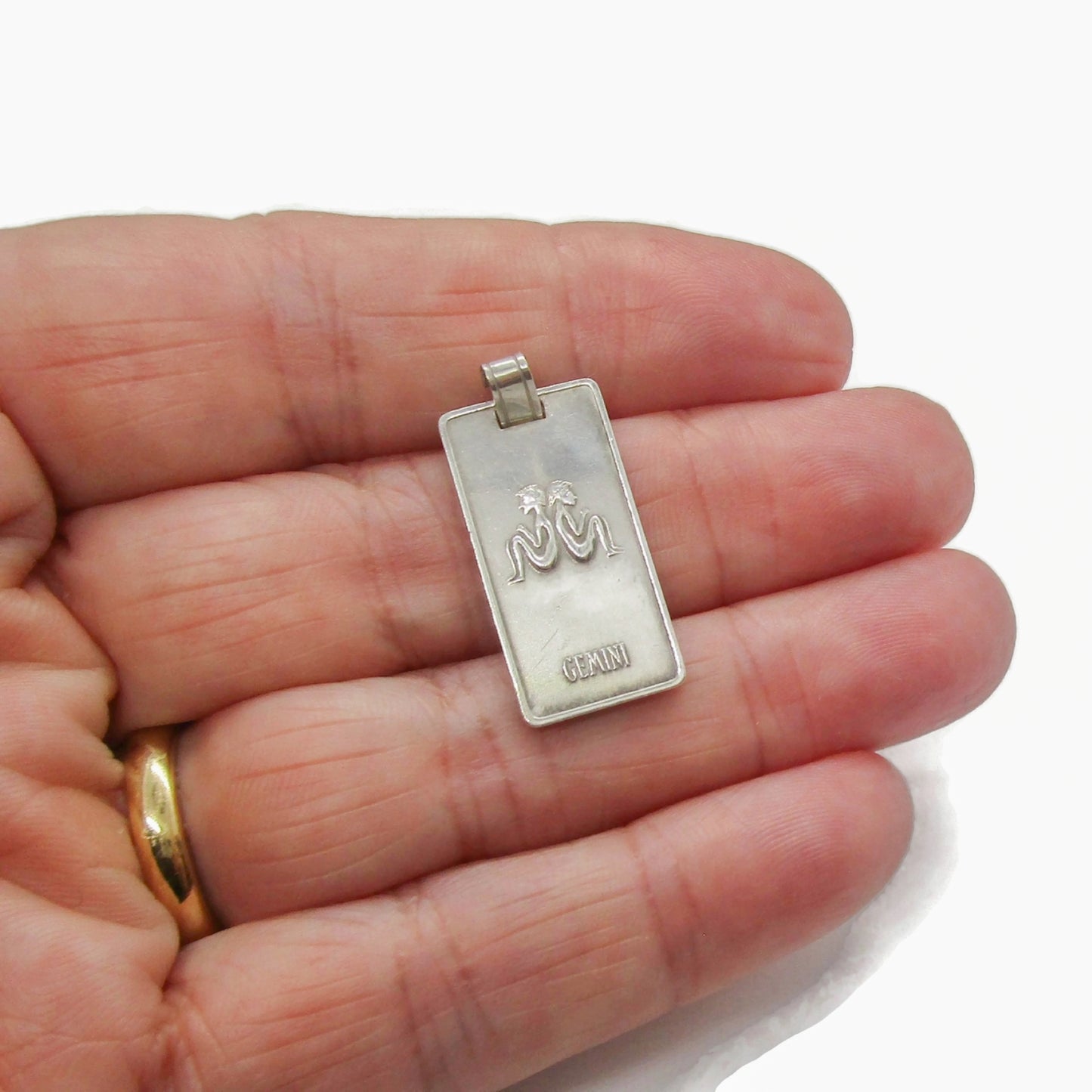 A Creola silver ingot Gemini pendant held in a hand
