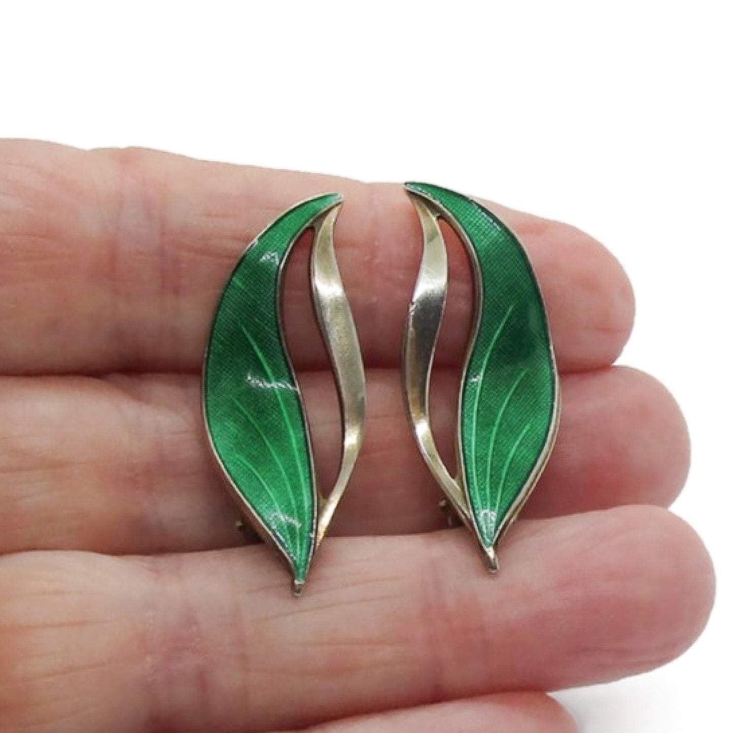 A pair of Hroar Prydz Norway green enamel and sterling silver gilt leaf shaped clip on earrings shown held in a hand