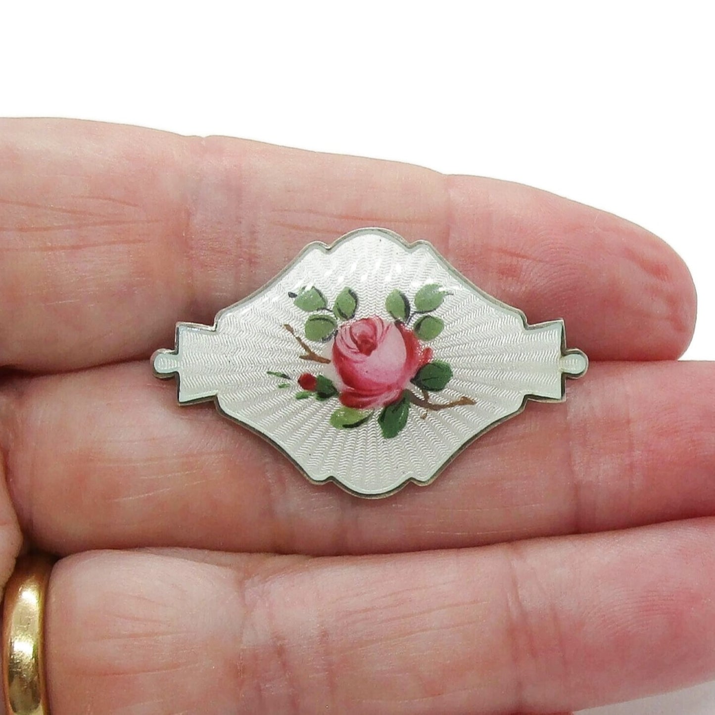 Small shield shaped Ivar Holth Norway sterling silver enamel pink rose brooch shown held in a hand