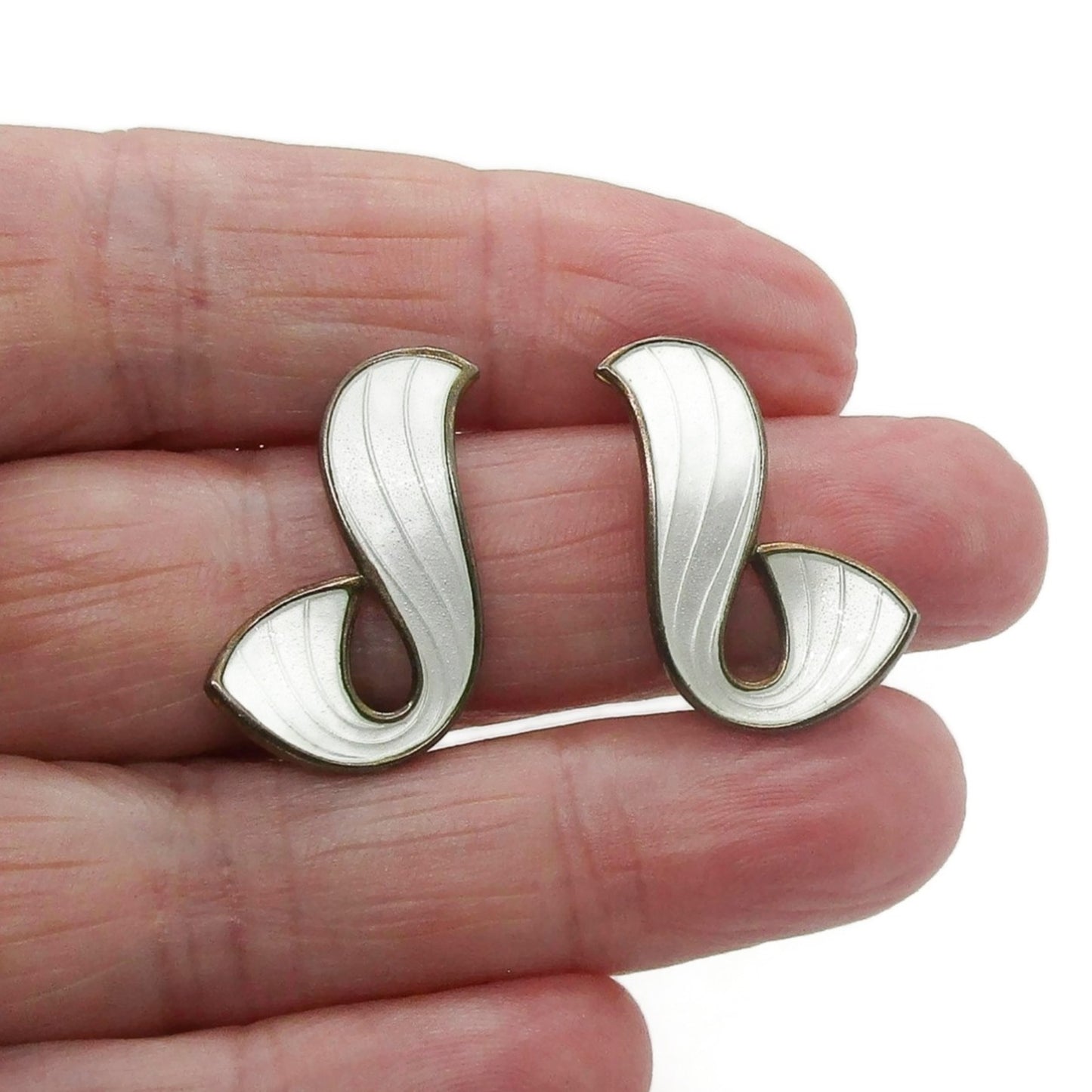 A pair of Ivar Holth Norway clip on earrings in sterling silver gilt and white guilloche enamel shown held ina hand