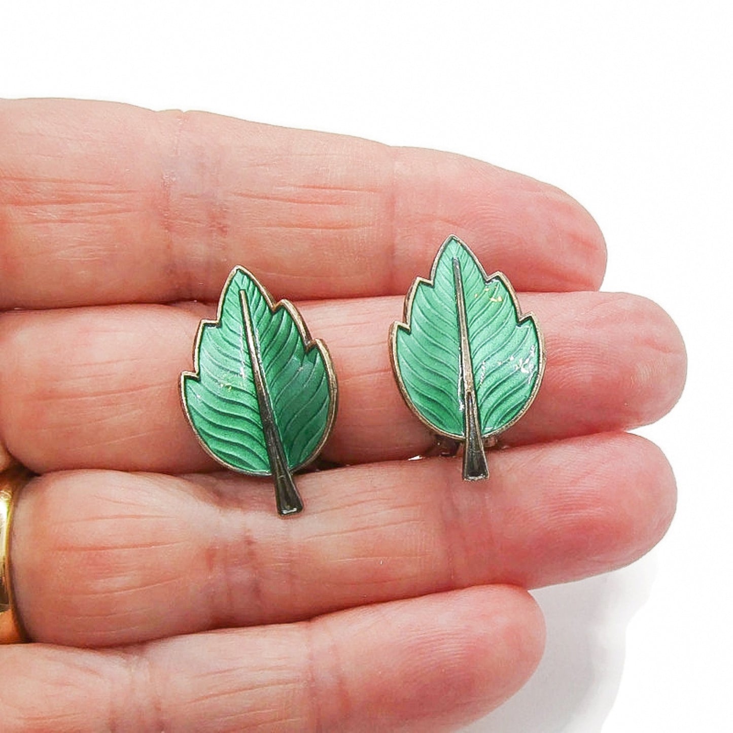 A pair of Jemax Denmark sterling silver and green enamel leaf clip on earrings shown held in a hand