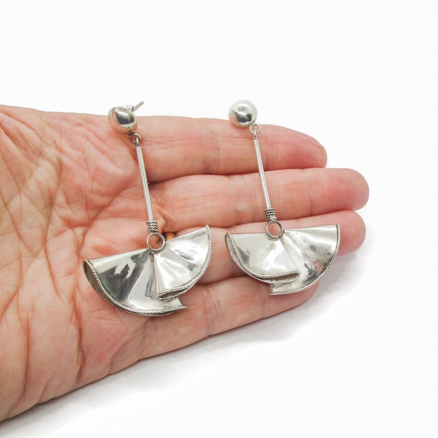 A pair of large sterling silver fan-shaped earrings for pierced ears shown held in a hand