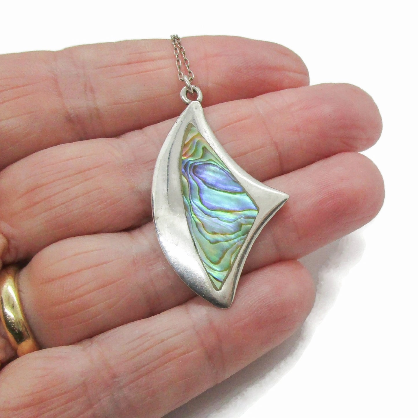 A vintage sterling silver and paua shell angular abstract pendant on a chain shown held in a hand