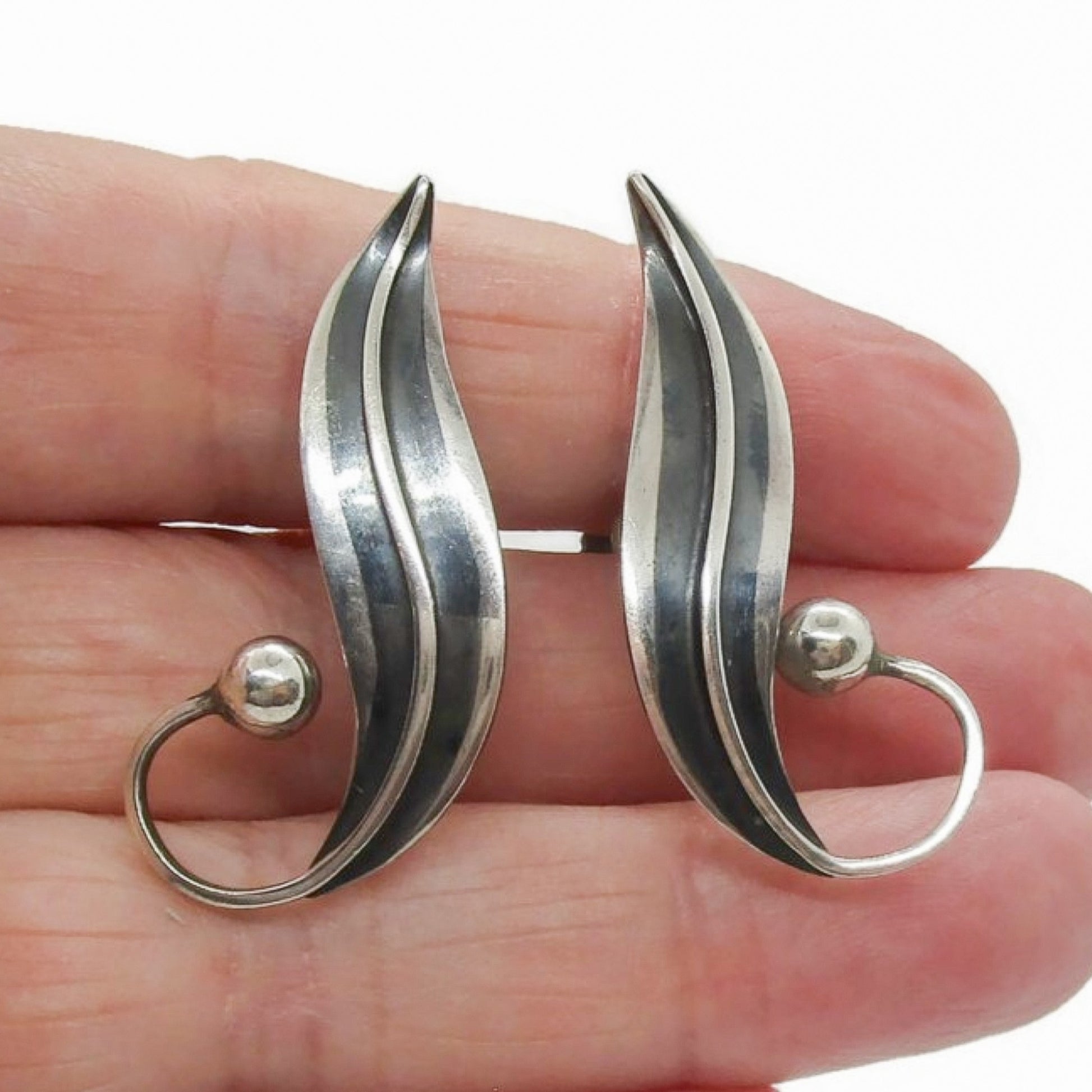 A pair of sterling silver screw on earrings in a curvy design by Delfino Mexico shown held in a hand