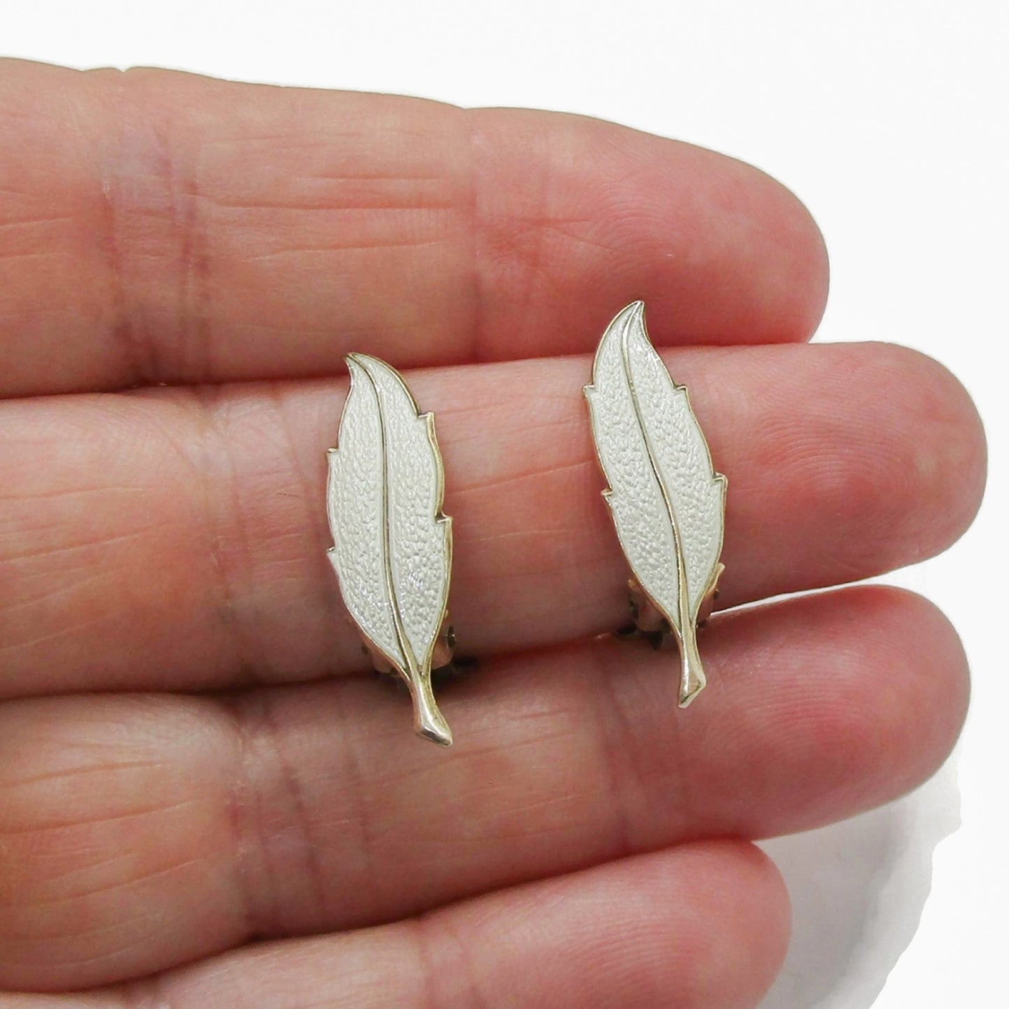 A pair of Finn Jensen Norway sterling silver gilt and white enamel leaf clip on earrings shown held in a hand