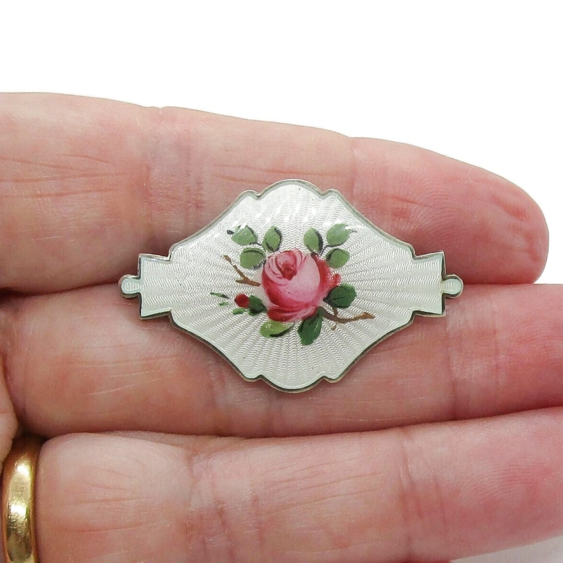 Small shield shaped Ivar Holth Norway sterling silver enamel pink rose brooch shown held in a hand