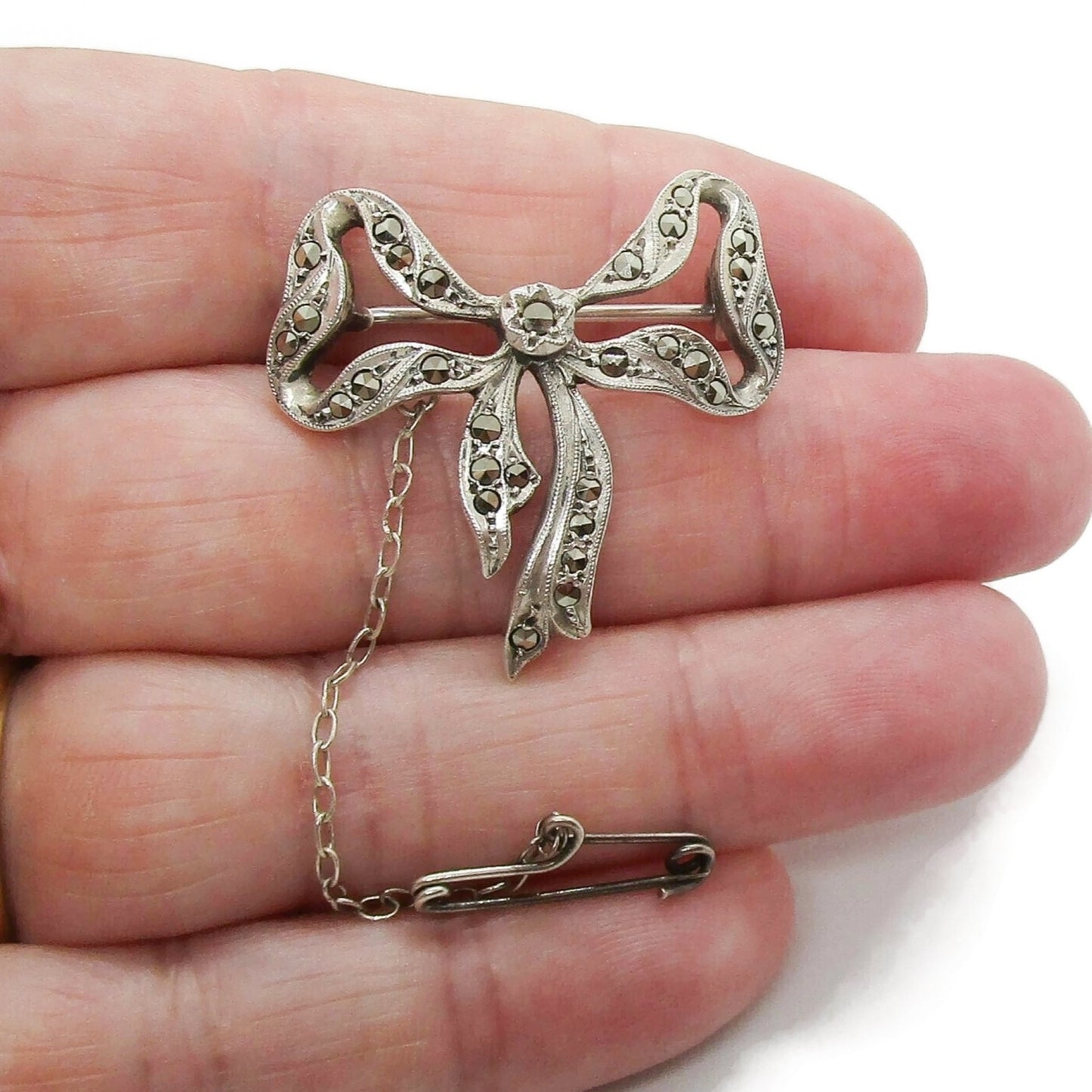 Lega Australia marcasite and sterling silver bow brooch with safety chain shown in a hand