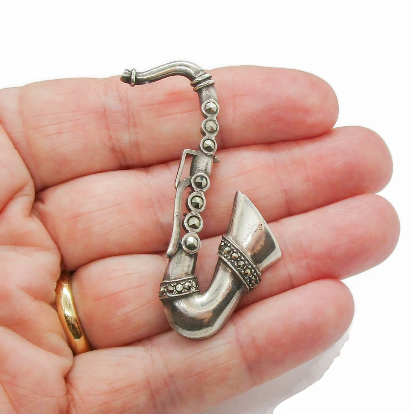 Vintage sterling silver and marcasite saxophone brooch shown in a hand