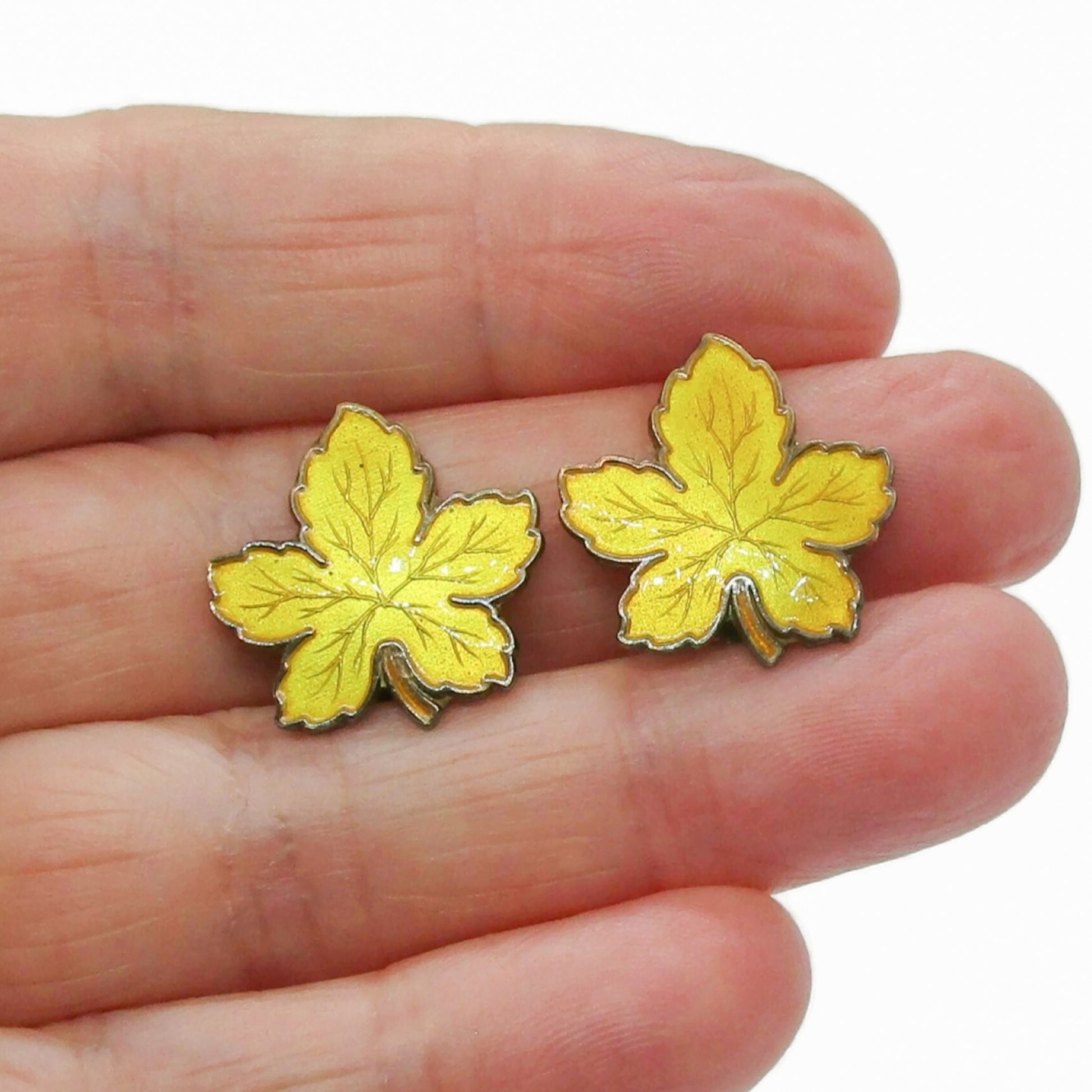 A pair of Meka Denmark yellow guilloche enamel and sterling silver gilt maple leaf clip on earrings shown held in a hand
