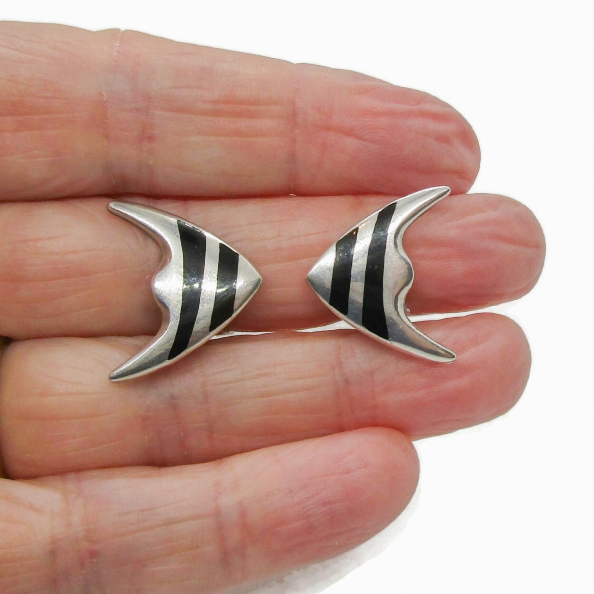 A pair of Meka sterling silver striped fish clip on earrings shown held in a hand