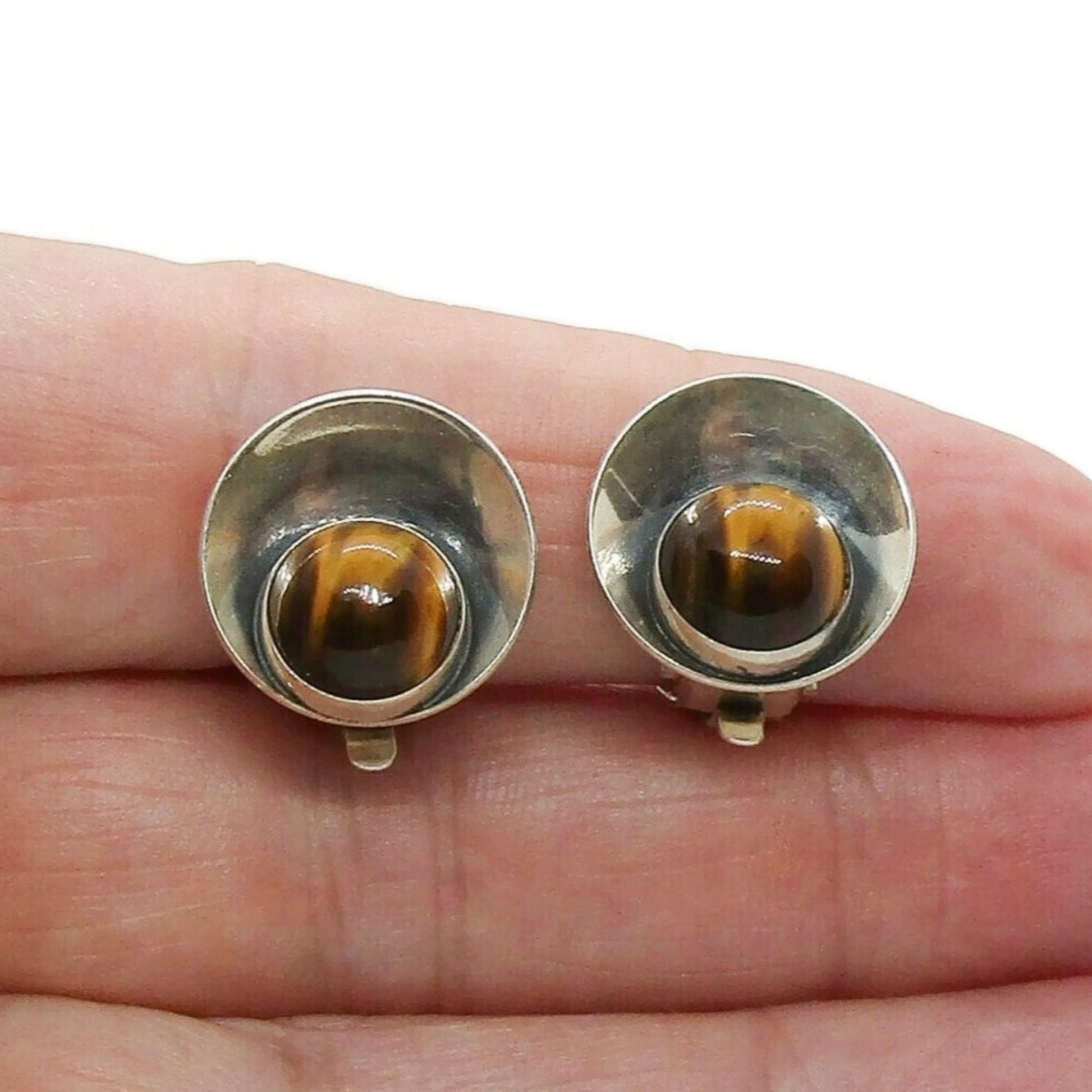 Pair of Niels Erik From Denmark sterling silver and tigers eye clip on earrings shown held in a hand