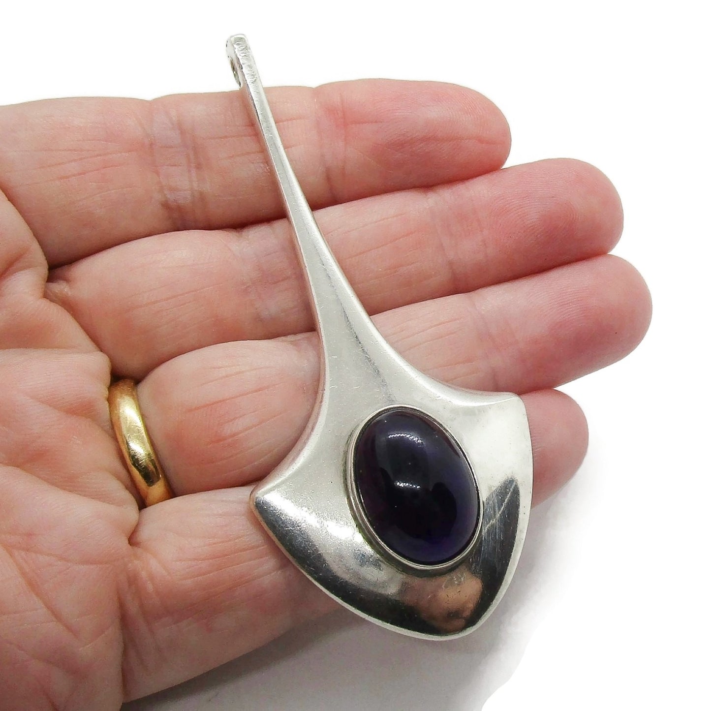A large vintage sterling silver and amethyst pendant shown held in a hand