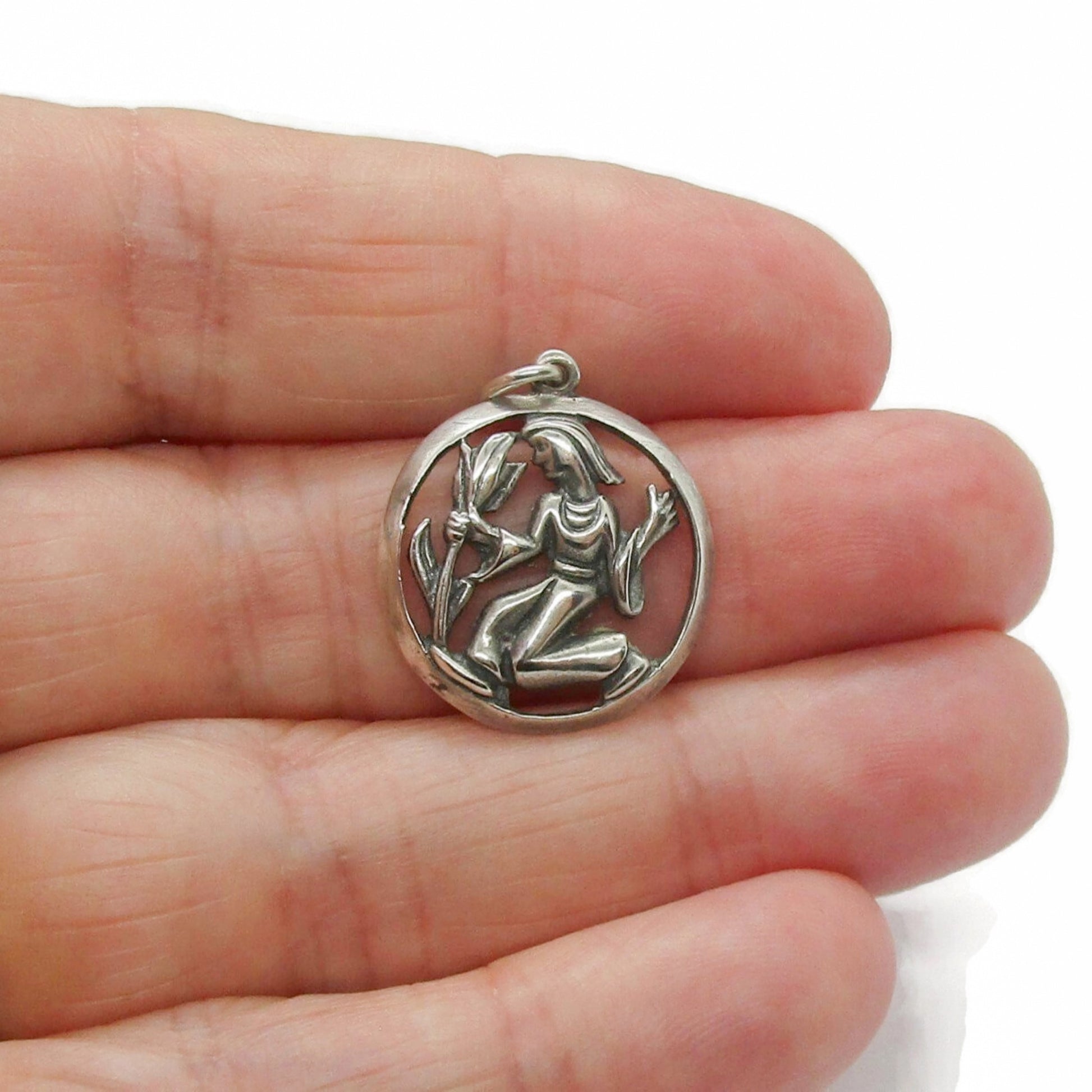 A vintage silver Virgo pendant held in a hand