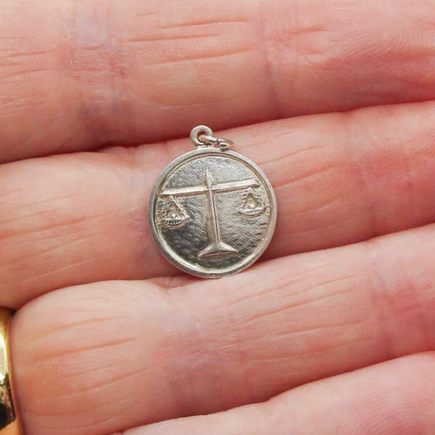 A small vintage sterling silver Libra pendant held in a hand