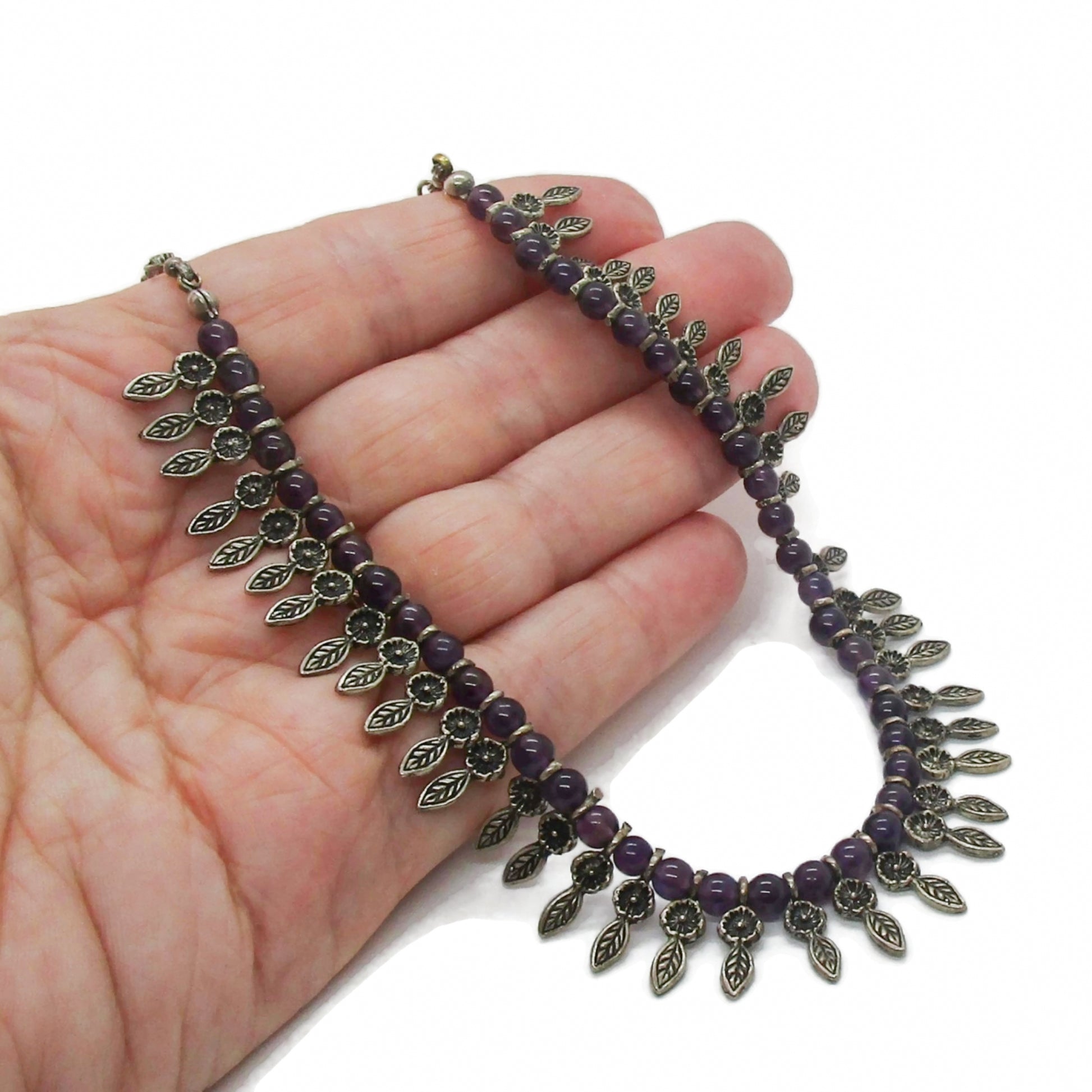 An amethyst bead and sterling silver leaf necklace held in a hand