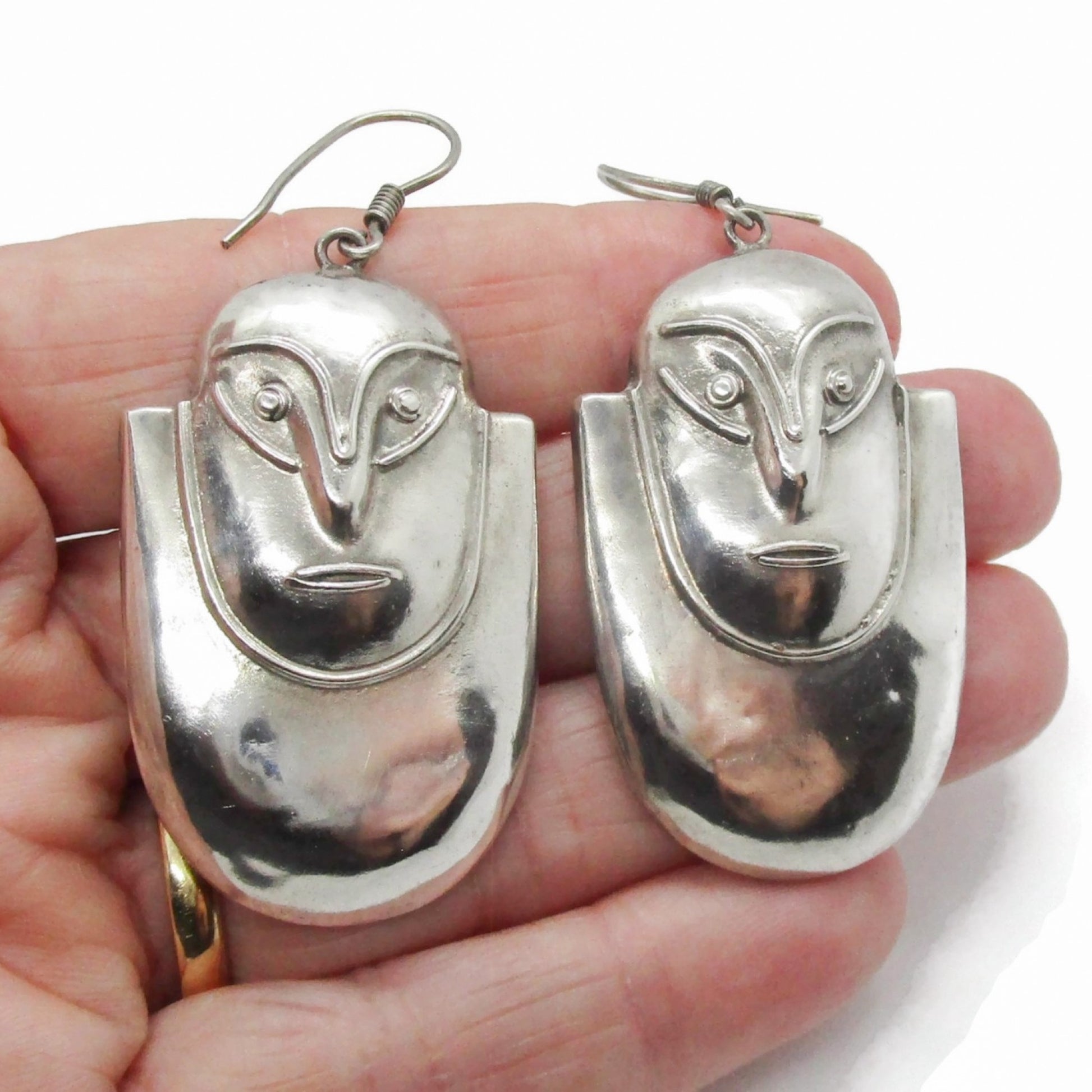 A pair of vintage big sterling silver face shaped dangle earrings shown held in a hand