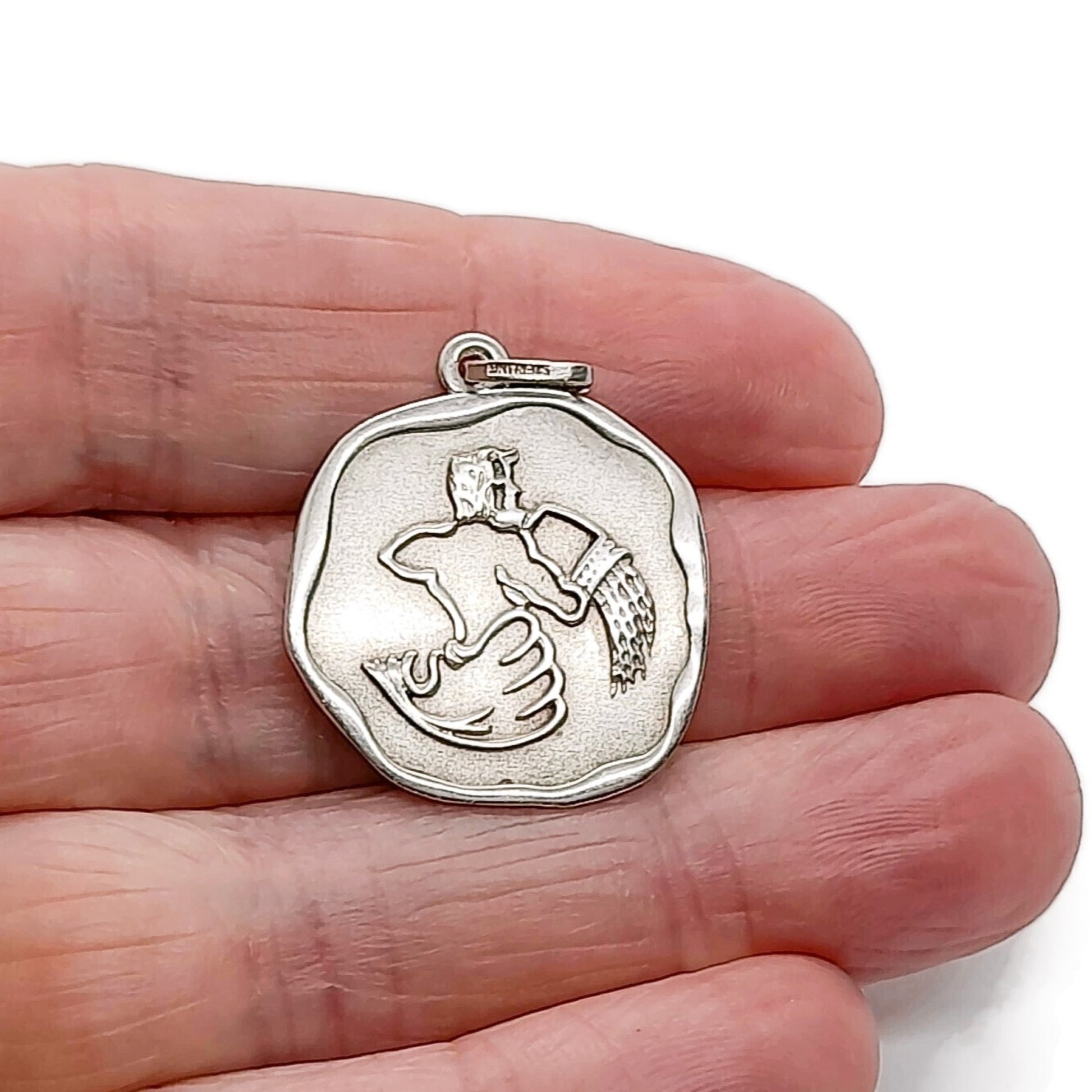 A vintage sterling silver Aquarius pendant held in a hand