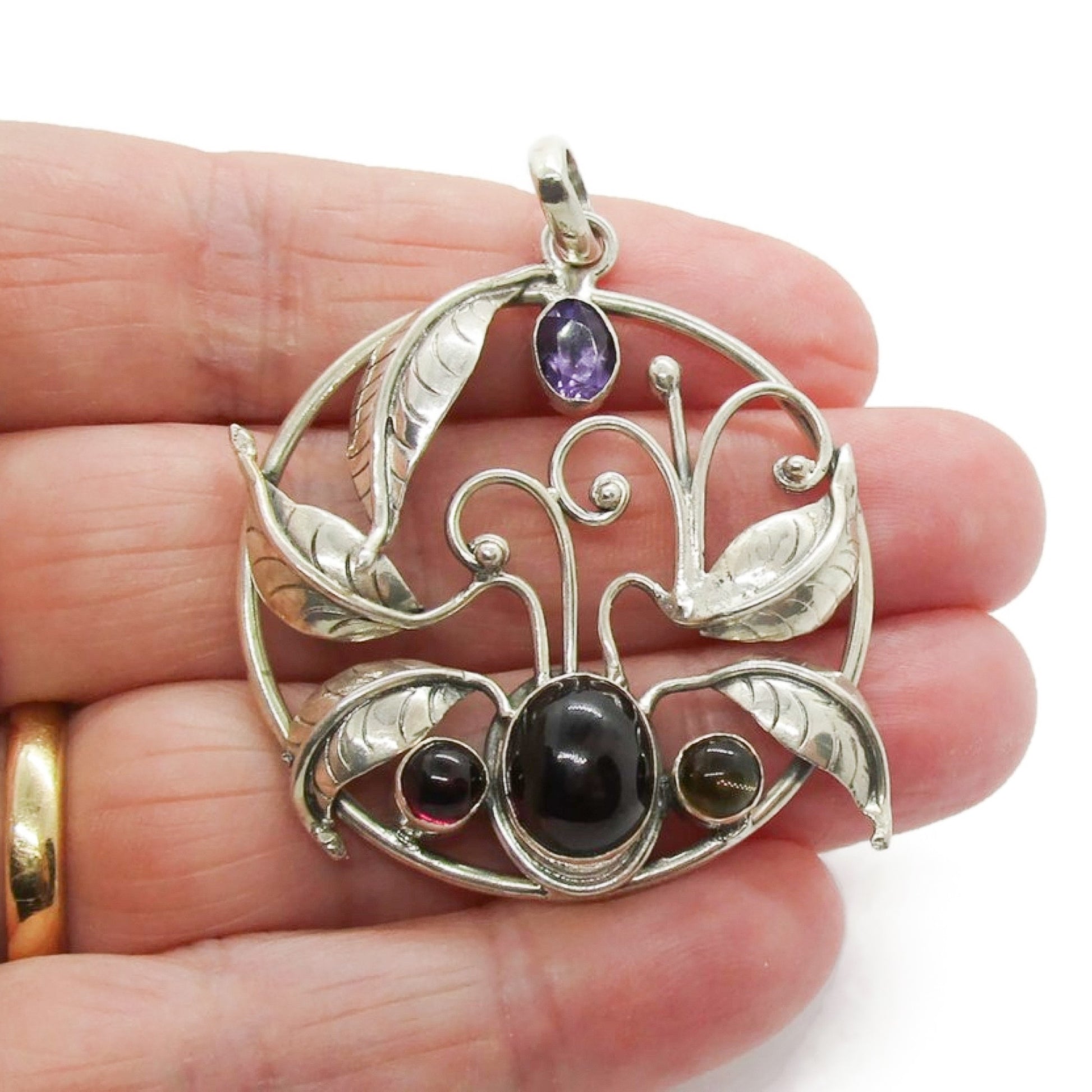 A large vintage sterling silver and gemstone floral design pendant held in a hand